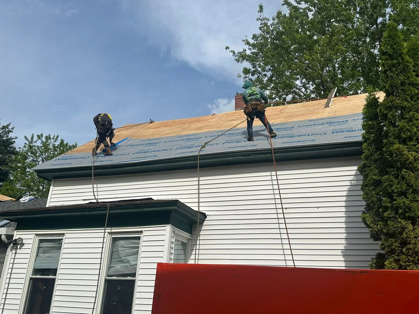Two of the crew working on a stripped roof deck, tied off, on a South Shore house